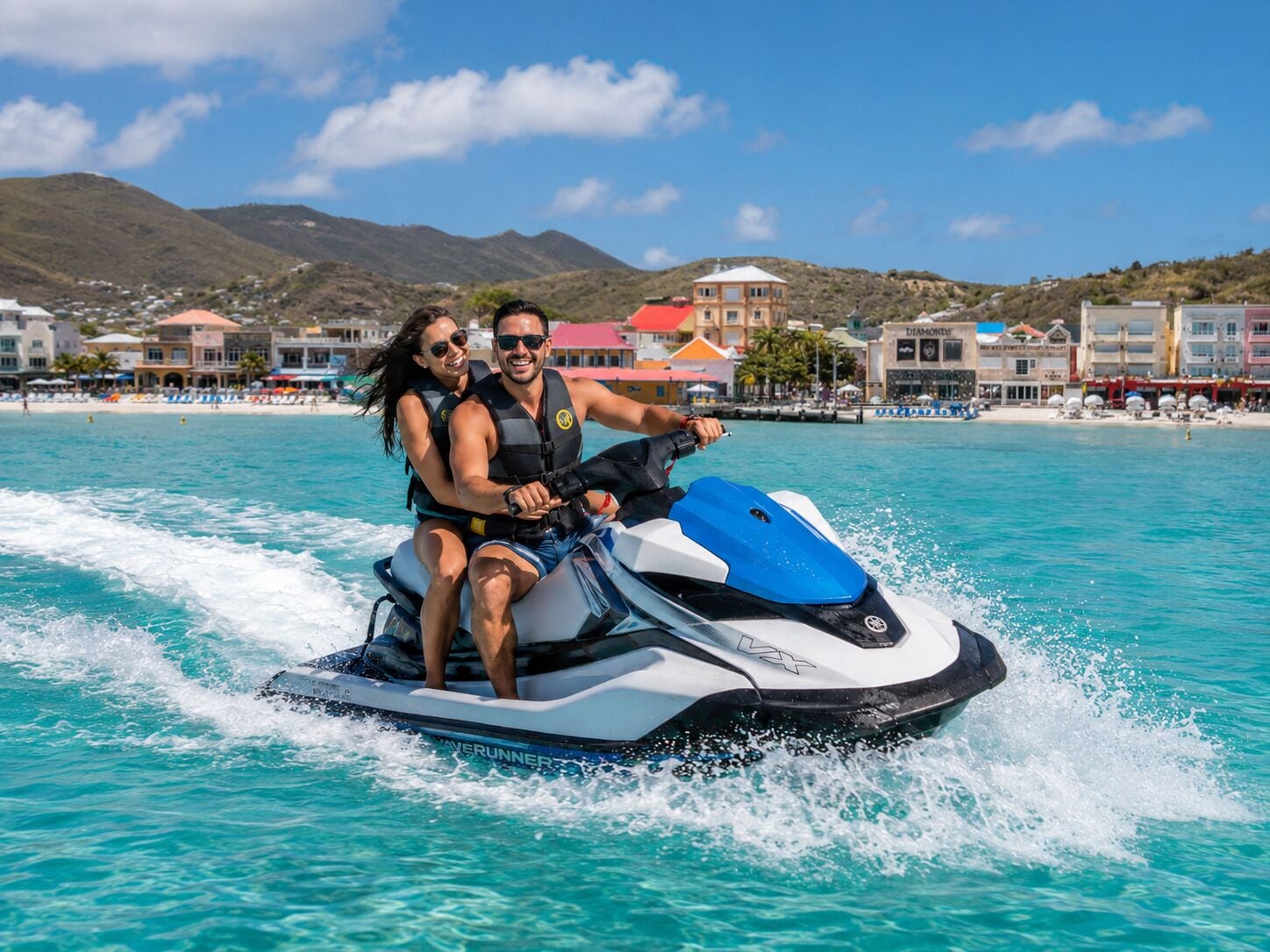 A jet ski on turquoise water with a mountainous backdrop and buildings.