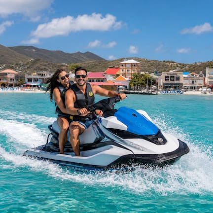 A jet ski on turquoise water with a mountainous backdrop and buildings.