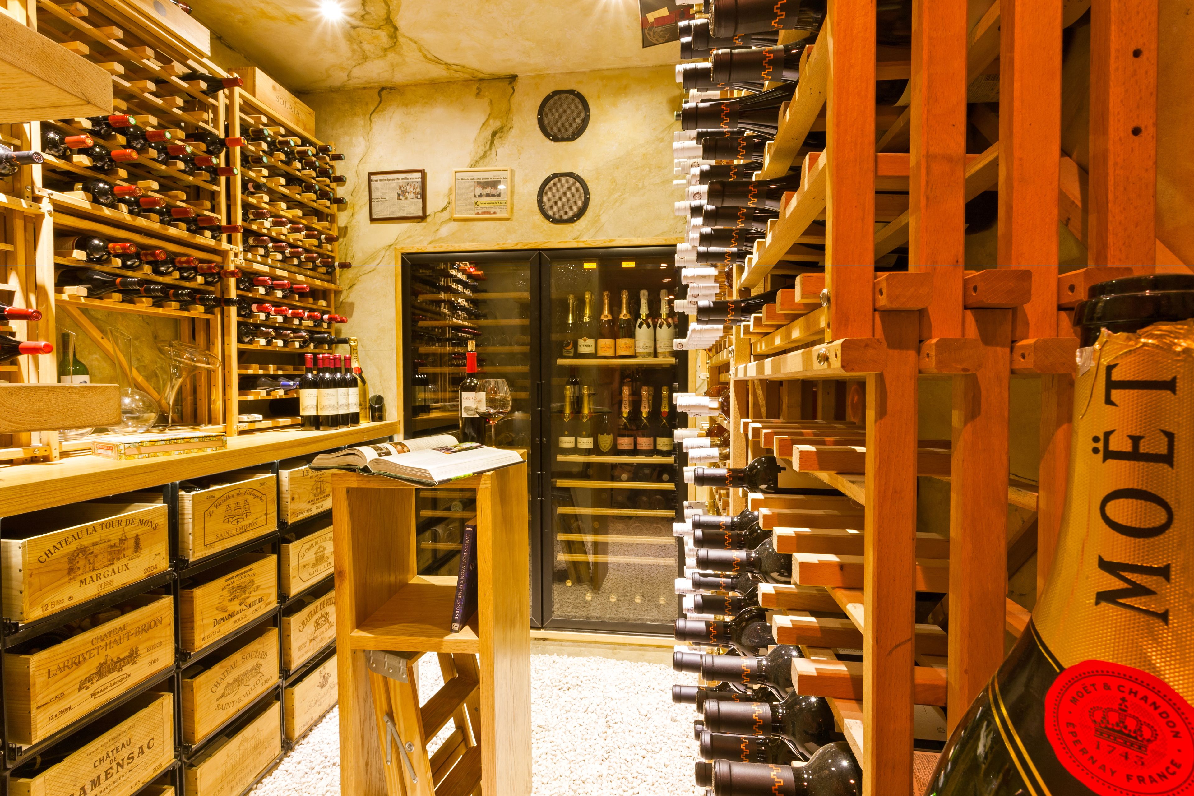 A wine cellar with wooden racks and shelves filled with wine bottles. There are wooden crates labeled with wine names and a glass cabinet.