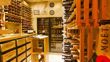 A wine cellar with wooden racks and shelves filled with wine bottles. There are wooden crates labeled with wine names and a glass cabinet.