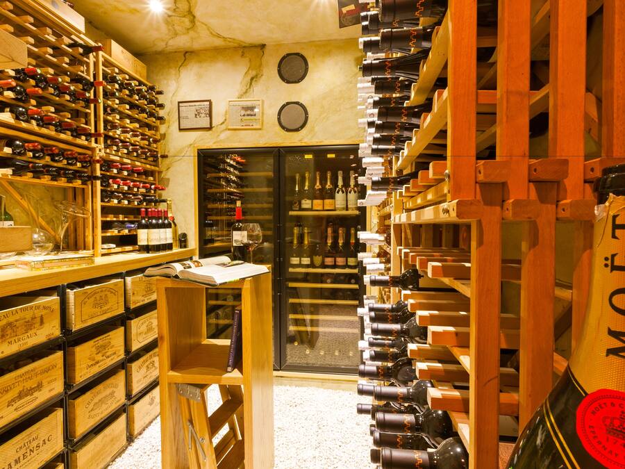A wine cellar with wooden racks and shelves filled with wine bottles. There are wooden crates labeled with wine names and a glass cabinet.