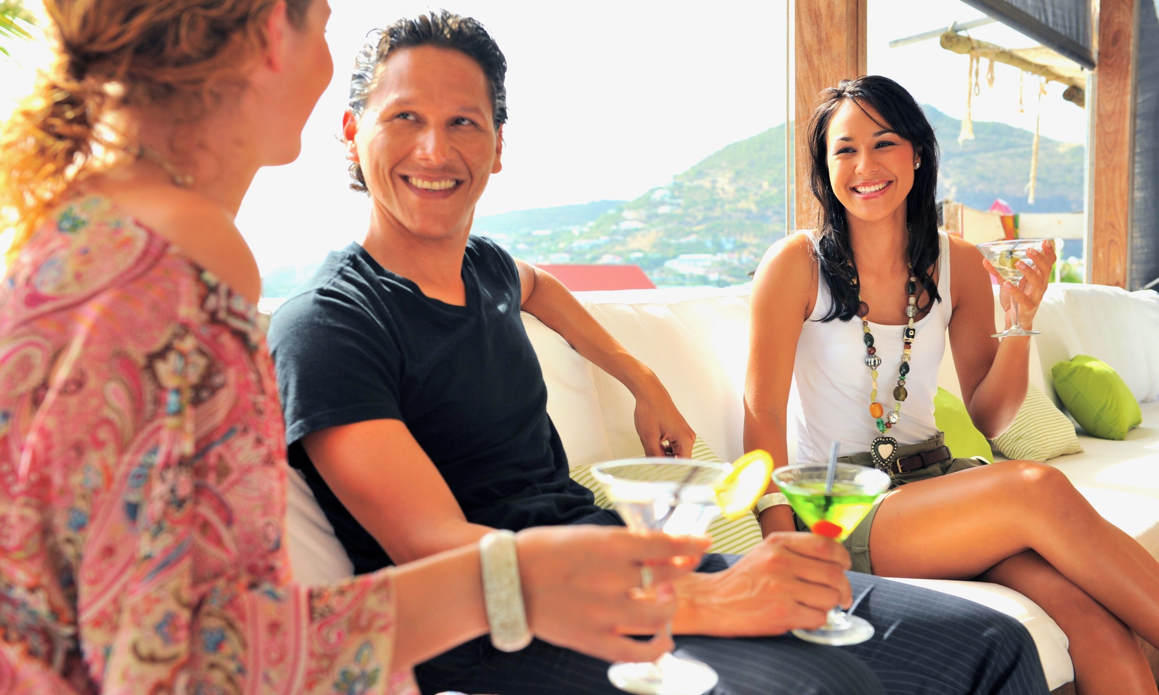 A group of people sitting on a white sofa with a view of a mountainous landscape.