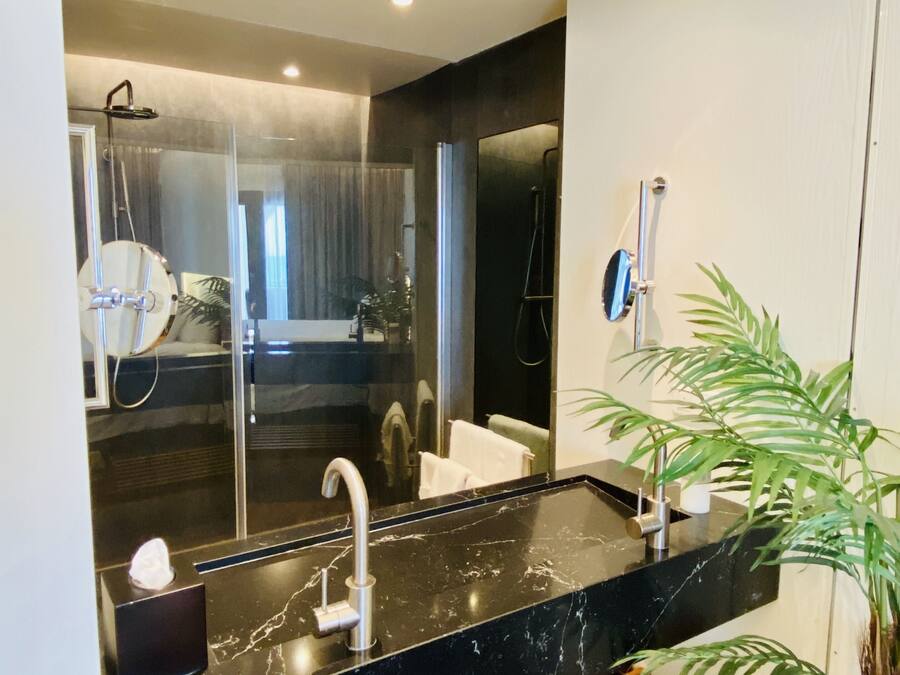 A modern bathroom with a large mirror, a black marble sink, and a wooden bench.