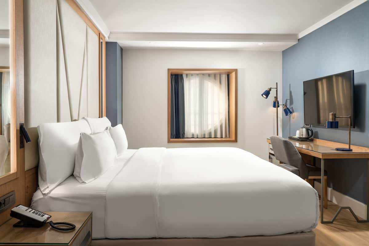 A hotel room with a large bed, a desk, a chair, a telephone, a television, and a window with curtains.