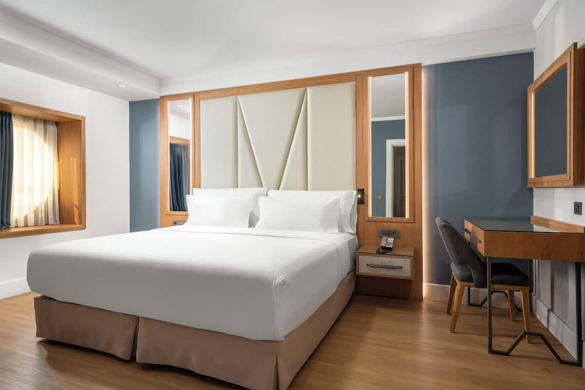 A modern hotel room with a large bed, a desk, and a mirror.