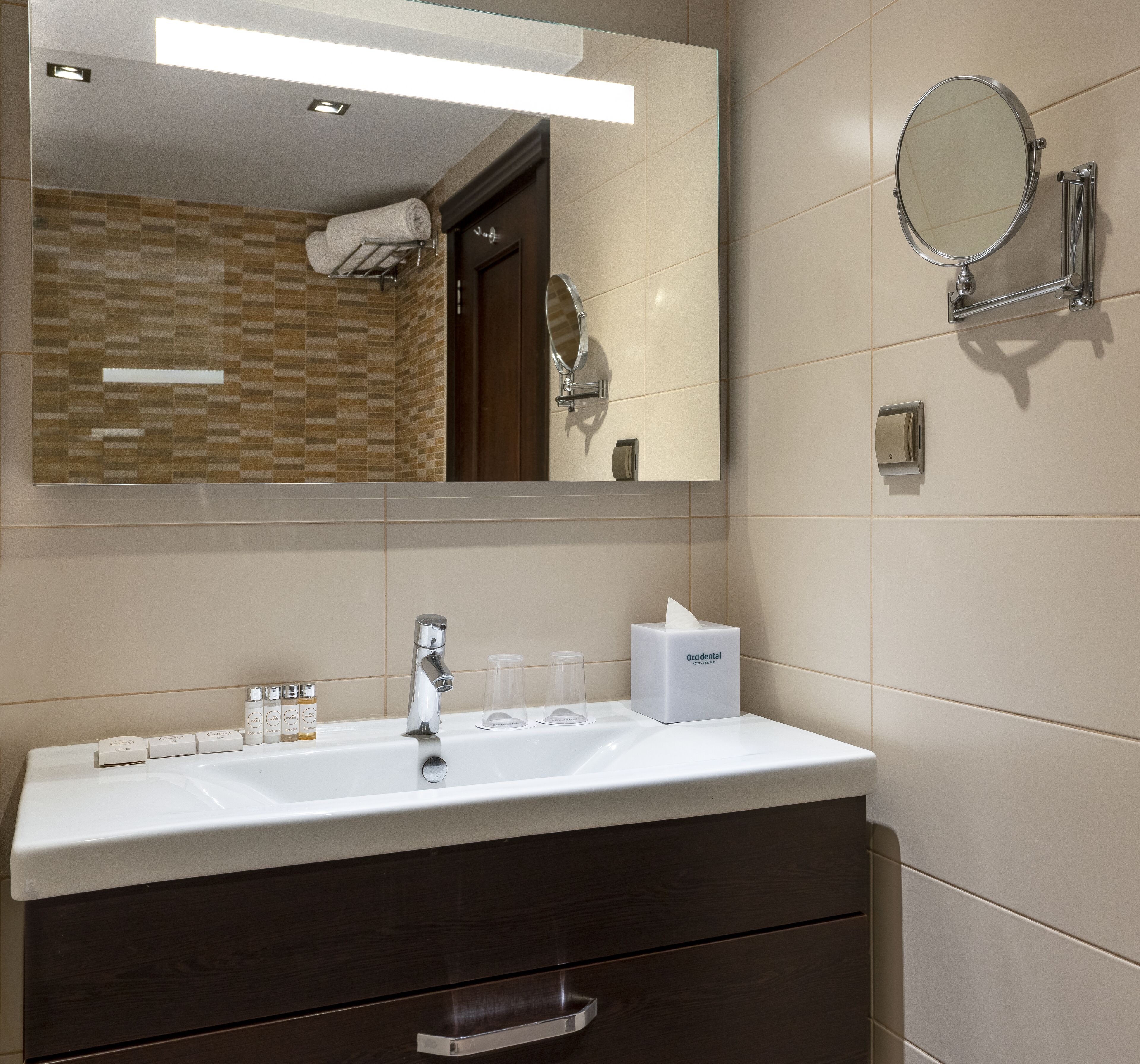 A modern bathroom with a white sink, a mirror, a towel rack, and toiletries.