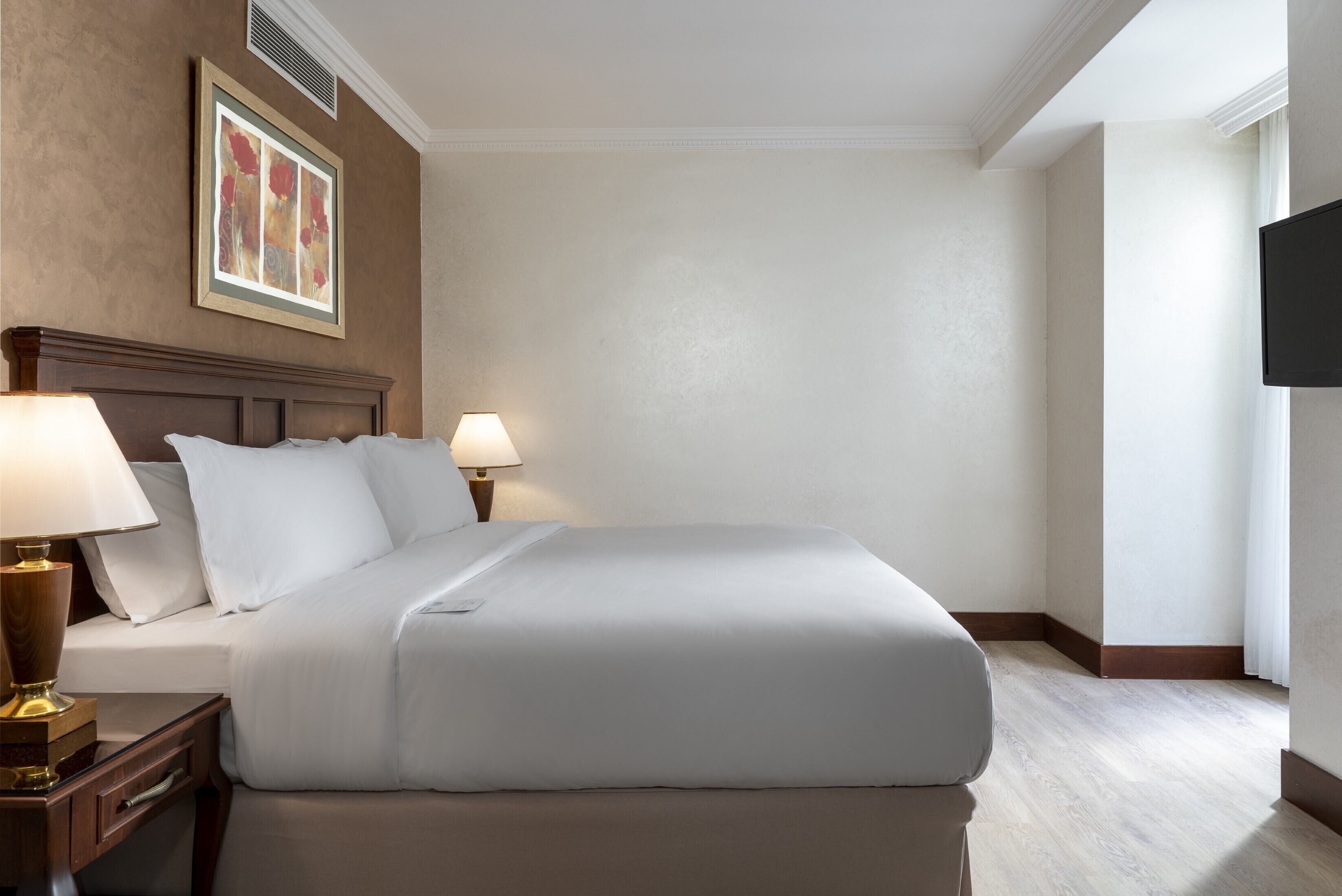 A neatly made bed with white linens, a wooden headboard, and two bedside lamps.