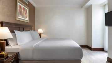 A neatly made bed with white linens, a wooden headboard, and two bedside lamps.