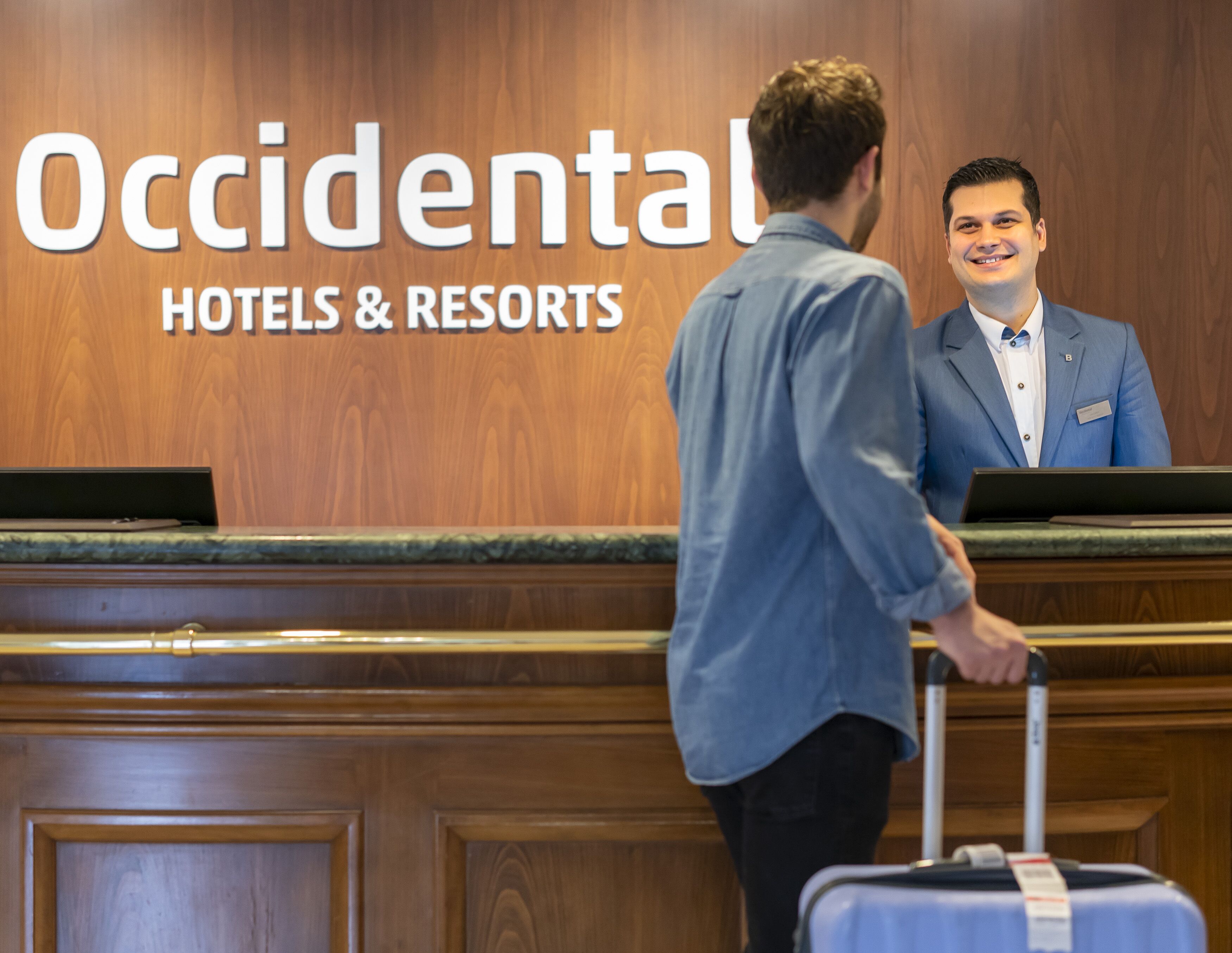 A hotel reception desk with a wooden panel background and a sign reading "Occidental Hotels & Resorts".