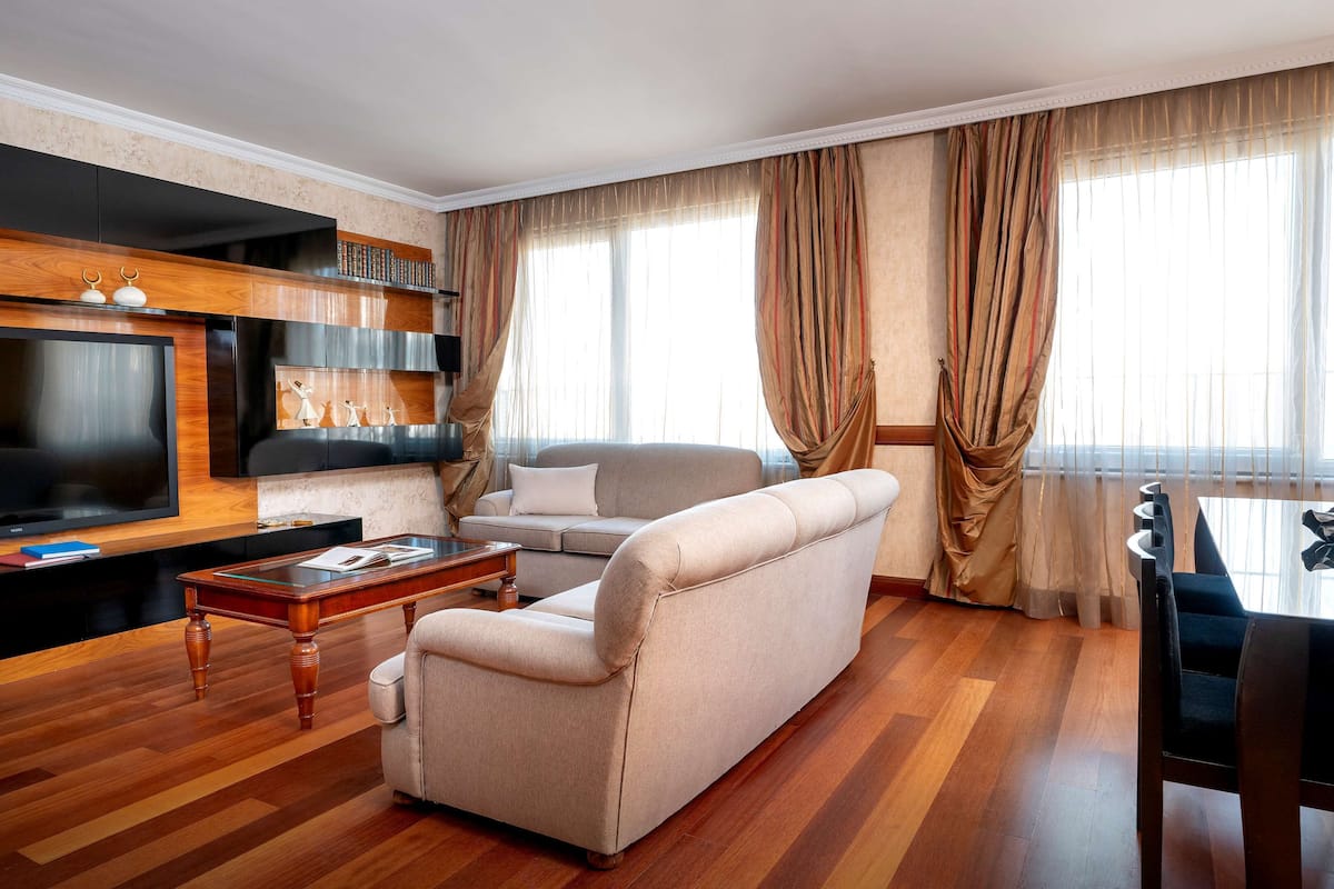 A modern living room with a flat-screen TV, a sofa, a coffee table, and a dining area with chairs.