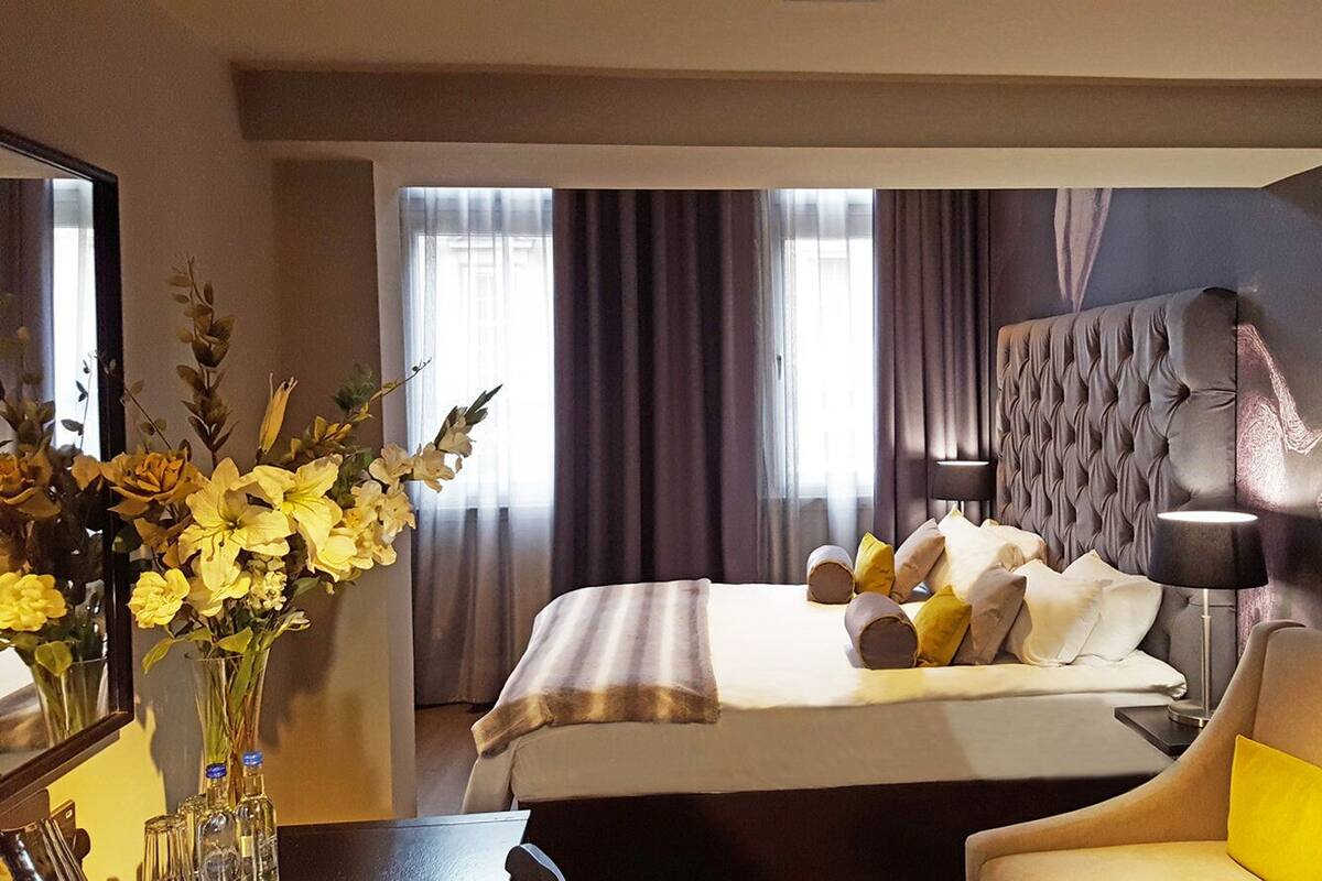 Ein Hotelzimmer mit einem großen Bett, einem Sessel, einem Blumenstrauß und einem Spiegel.