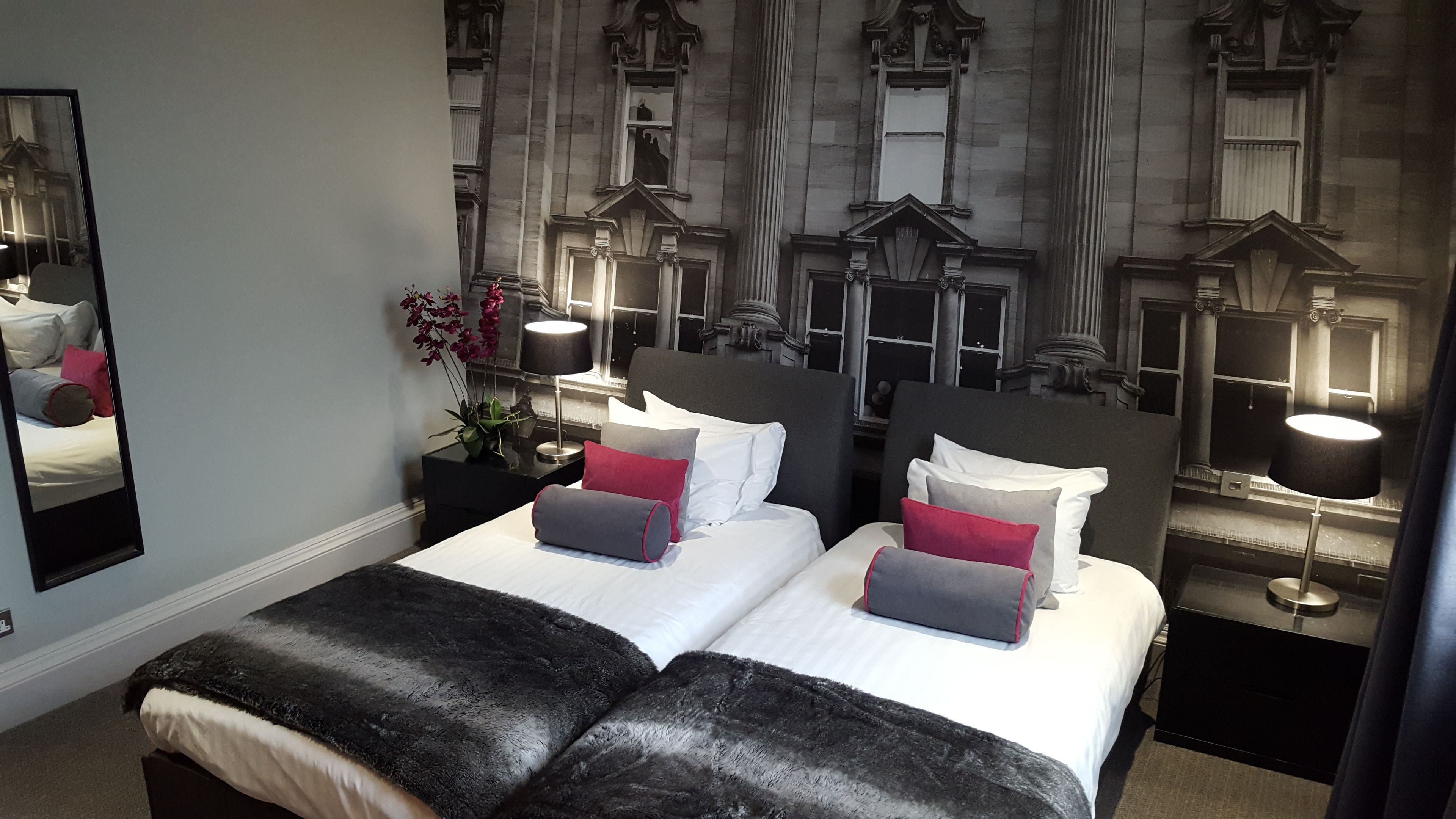 A hotel room with a large bed, two bedside tables, a mirror, and a wall with a detailed mural.