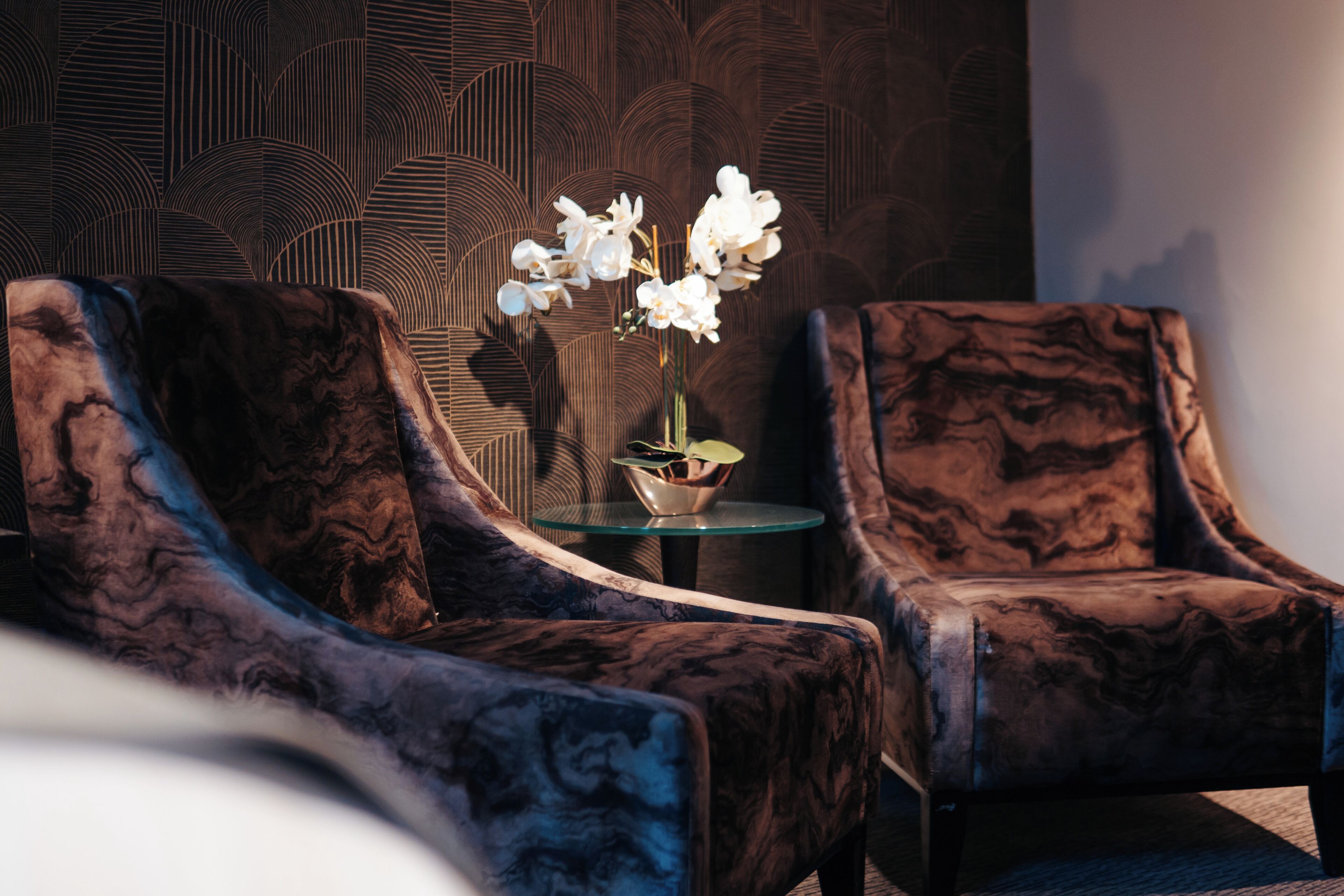 A room with two armchairs and a small table with a vase of white flowers.