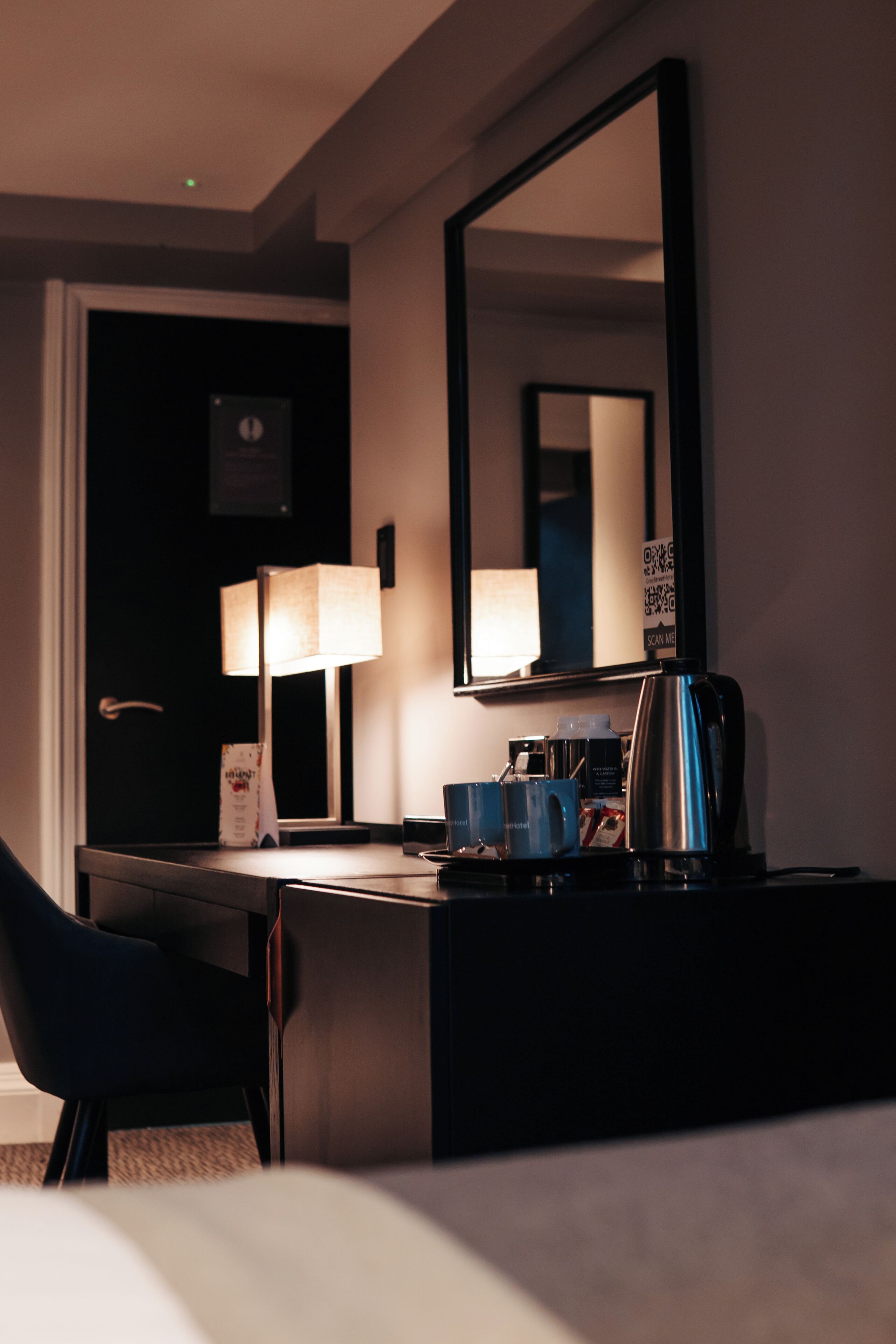 Una habitación de hotel con escritorio, silla, lámpara, cafetera y espejo.