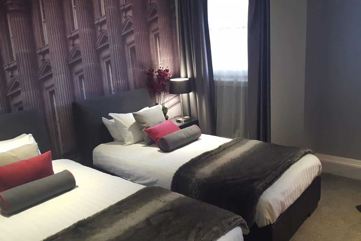 Ein Hotelzimmer mit Bett, Nachttisch, Lampe und einem roten Sessel.