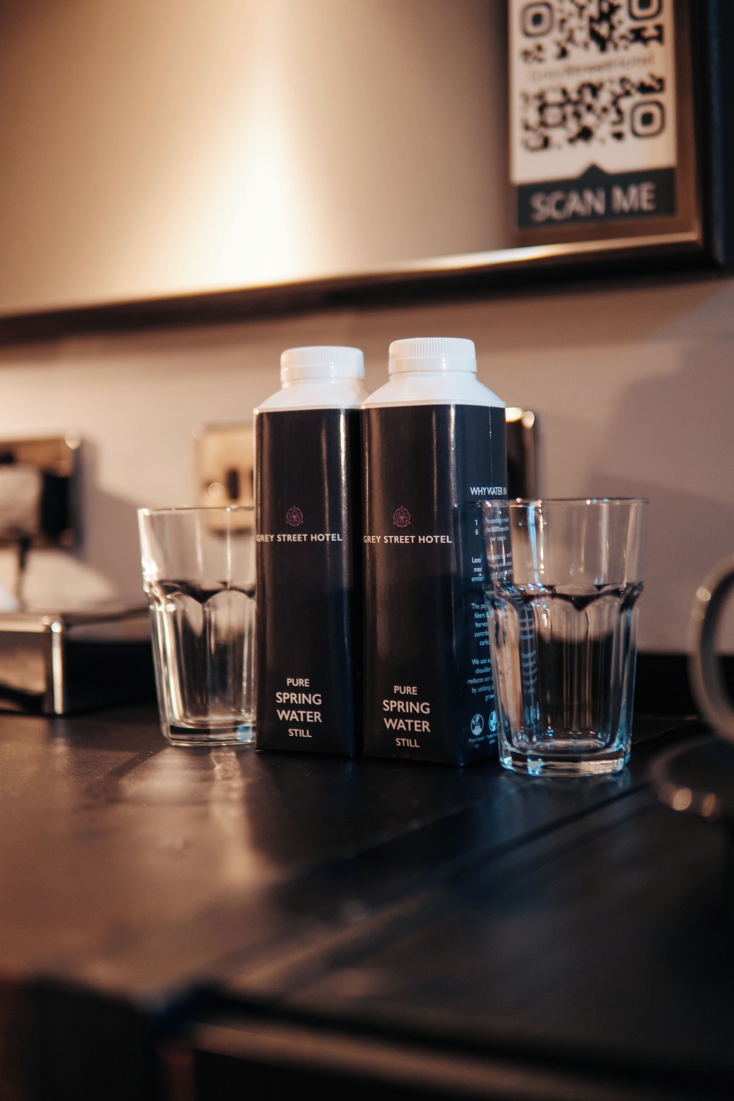 Two bottles of Grey Street Hotel's Pure Spring Water and two glasses on a table.