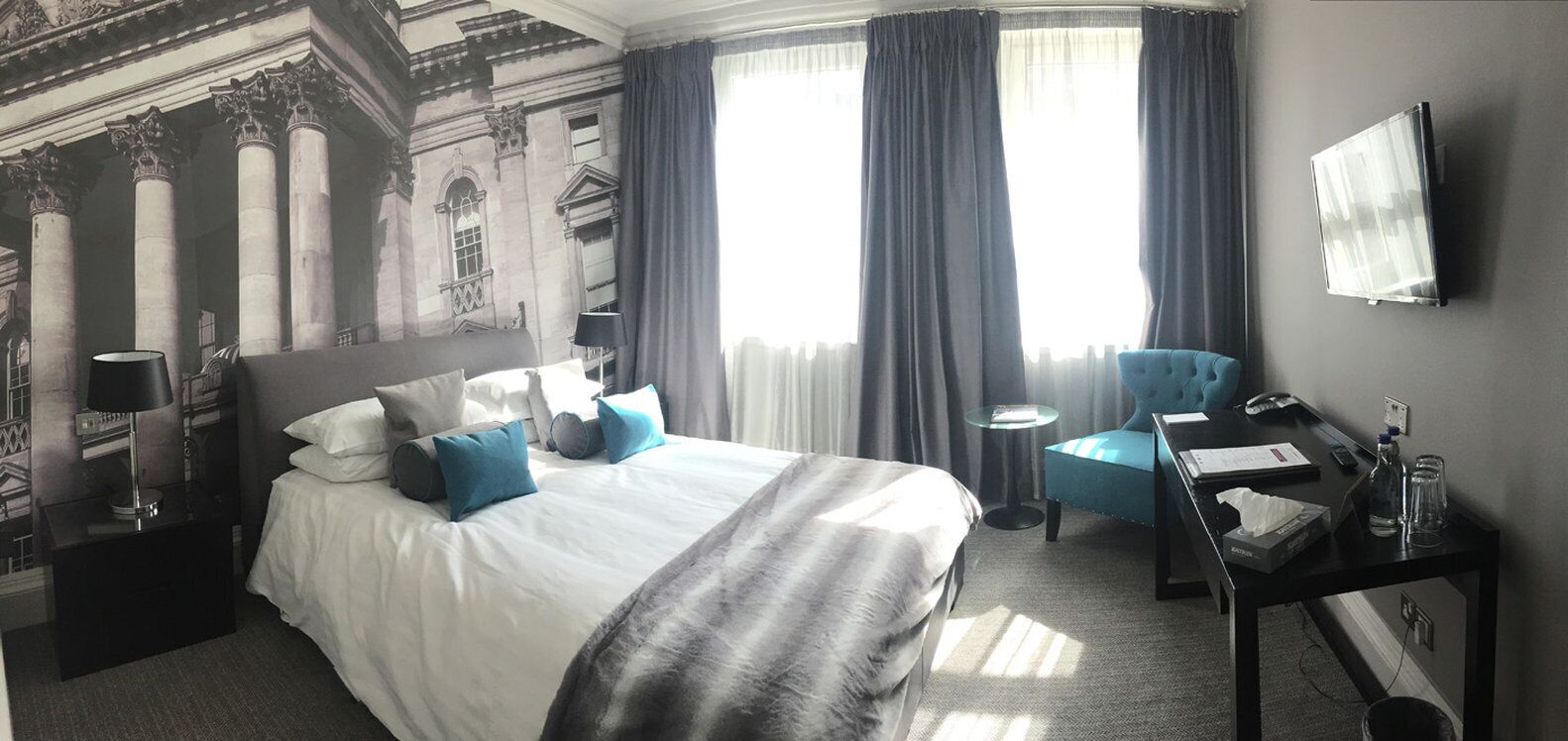 A hotel room with a large bed, a desk, a chair, and a TV.