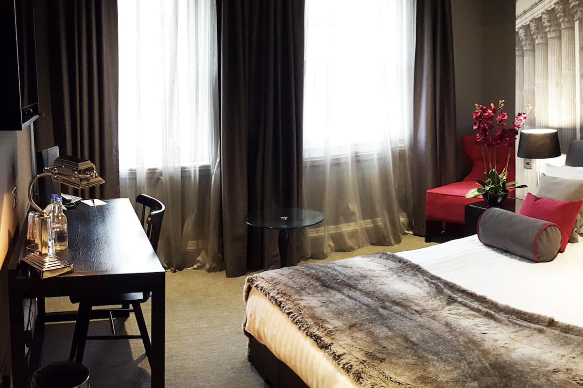 Ein Hotelzimmer mit einem großen Bett, einem Schreibtisch, einem Sessel, einer Lampe und einem Kamin.
