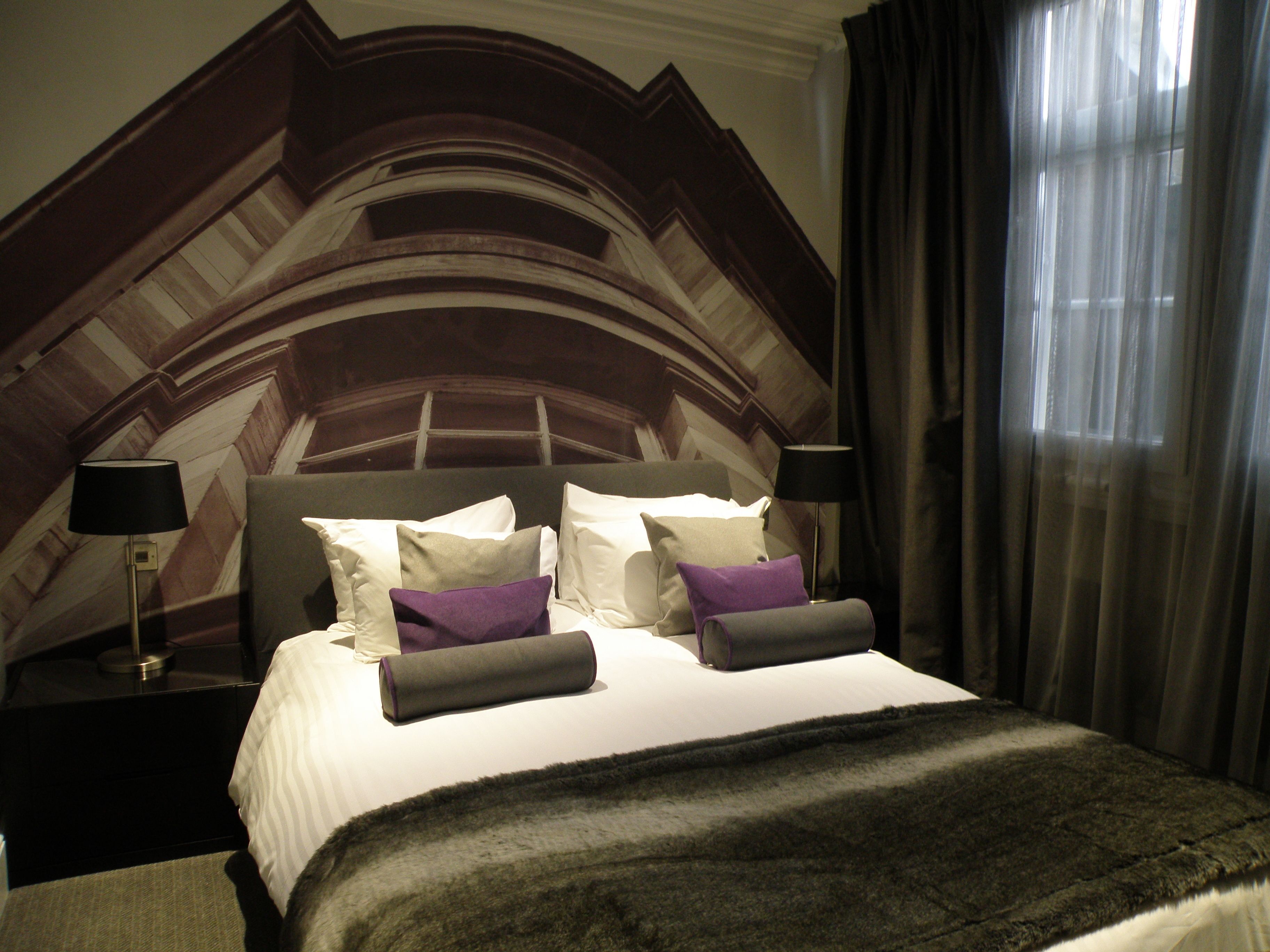 Habitación de hotel con una cama grande, dos mesitas de noche, un cabecero y una ventana con cortinas.