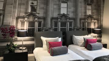 A hotel room with two beds, a large window, and a mural of a building facade.