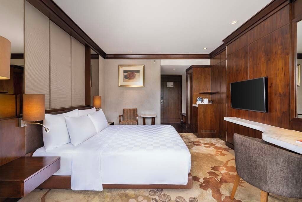 A hotel room with a large bed, a TV mounted on the wall, a desk, and a chair.