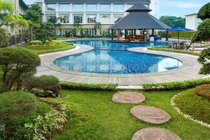 A large, circular swimming pool with a wooden deck surrounding it, set in a landscaped garden with various plants and a gazebo in the background. - Swiss-Belhotel Borneo Banjarmasin (Banjarmasin)