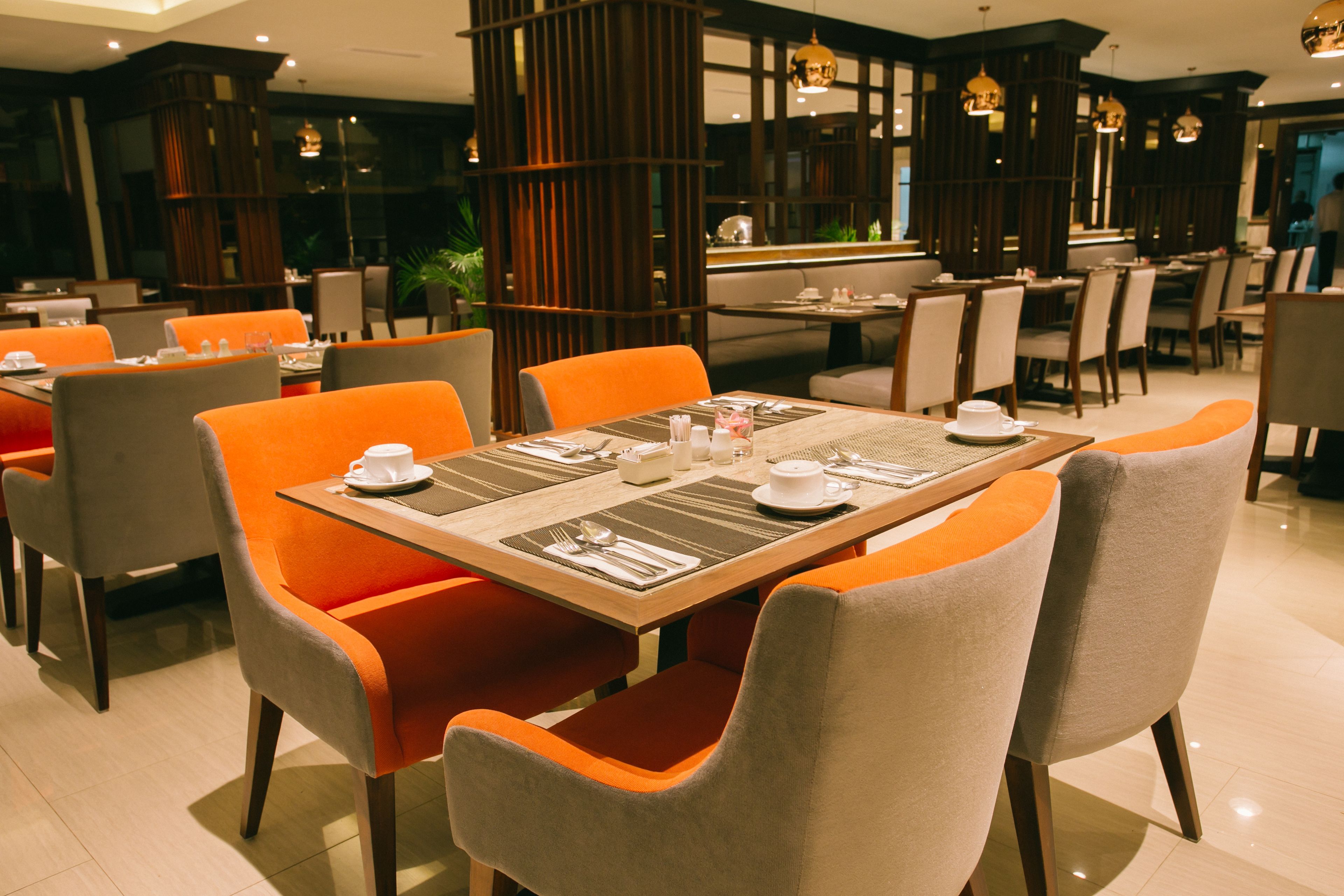 Un restaurant amb taules preparades per dinar, amb una combinació de cadires taronges i grises.