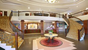 A grand lobby with a central round table, a staircase with ornate railings, and a second-floor balcony. - Swiss-Belhotel Borneo Banjarmasin (Banjarmasin)