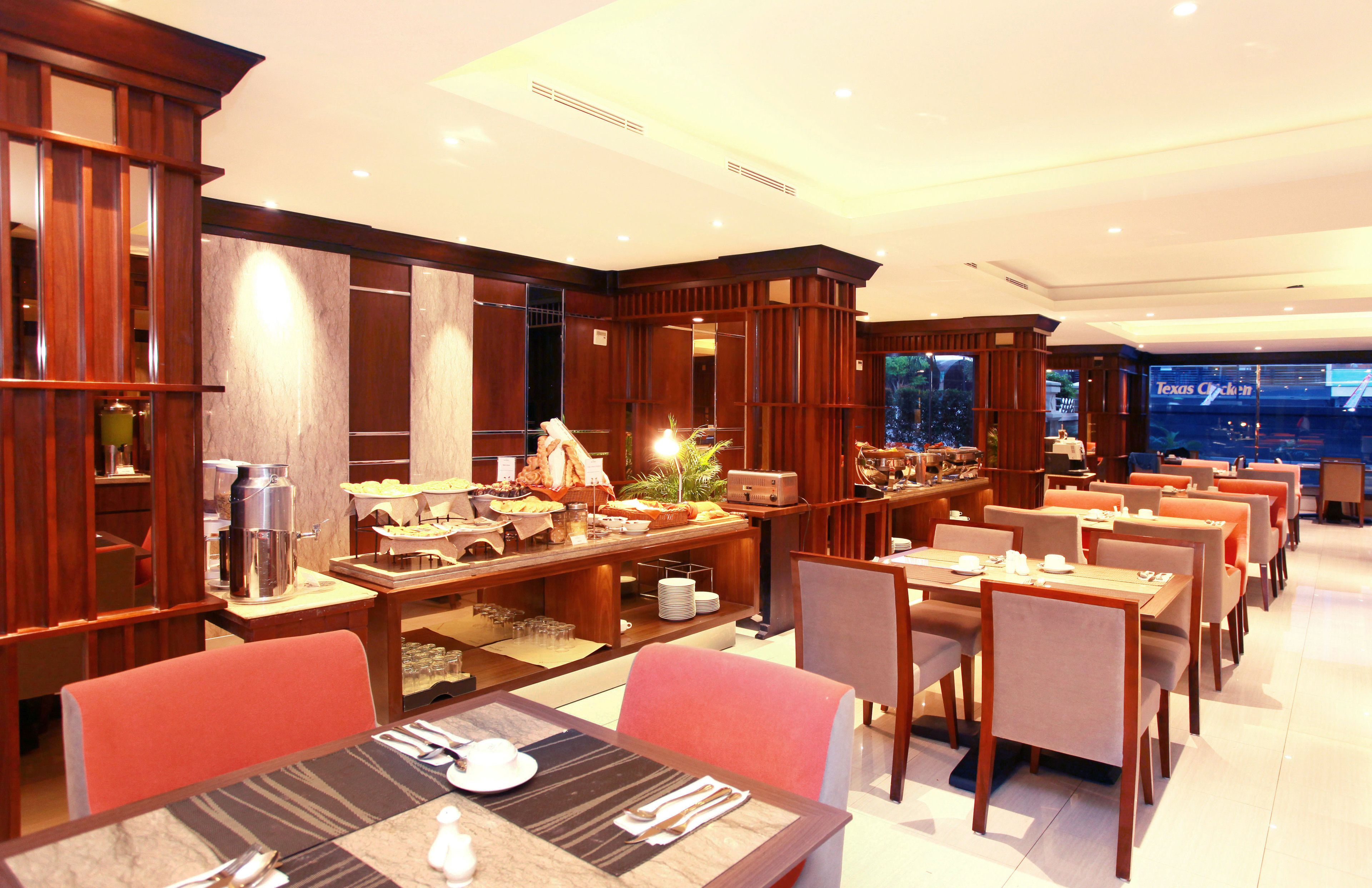 Een restaurantgedeelte in een hotel met meerdere tafels en stoelen, een buffetopstelling en een groot raam met uitzicht op de stad.