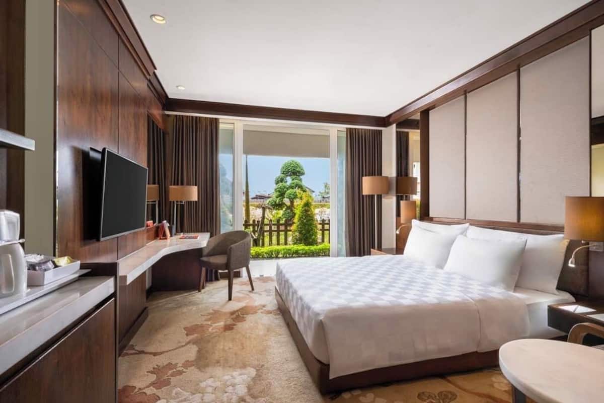 Une chambre d’hôtel dotée d’un grand lit, d’un bureau avec un téléviseur à écran plat, d’une chaise et offrant une vue sur un jardin grâce à une porte coulissante.