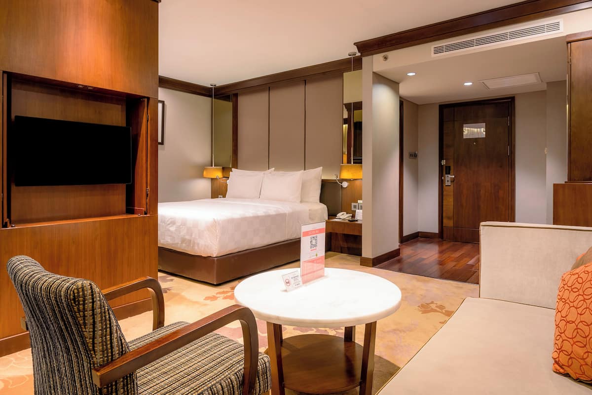 Une chambre d’hôtel comprenant un lit, un bureau avec une lampe, une chaise, une table ronde et un téléviseur fixé au mur.