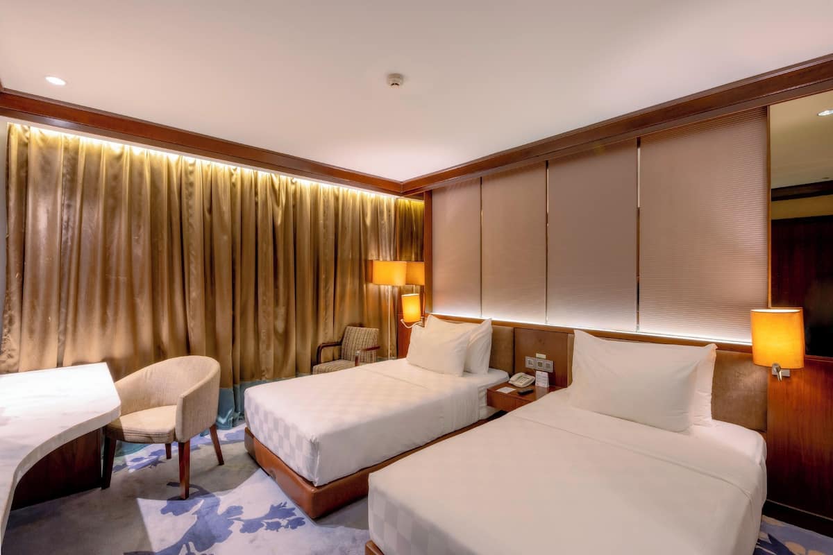Une chambre d’hôtel avec deux lits, un bureau, une chaise et une grande fenêtre avec des rideaux.
