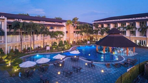 A hotel with a swimming pool, outdoor seating, and palm trees. - Swiss-Belhotel Borneo Banjarmasin (Banjarmasin)