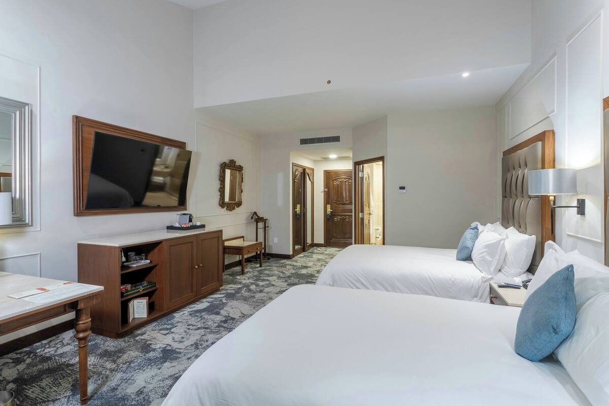 A hotel room with two beds, a desk, a television, and a wardrobe.