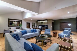 Uma sala de estar espaçosa com um sofá cinza, poltronas azuis, uma mesa de centro e um espaço de jantar com um candelabro.