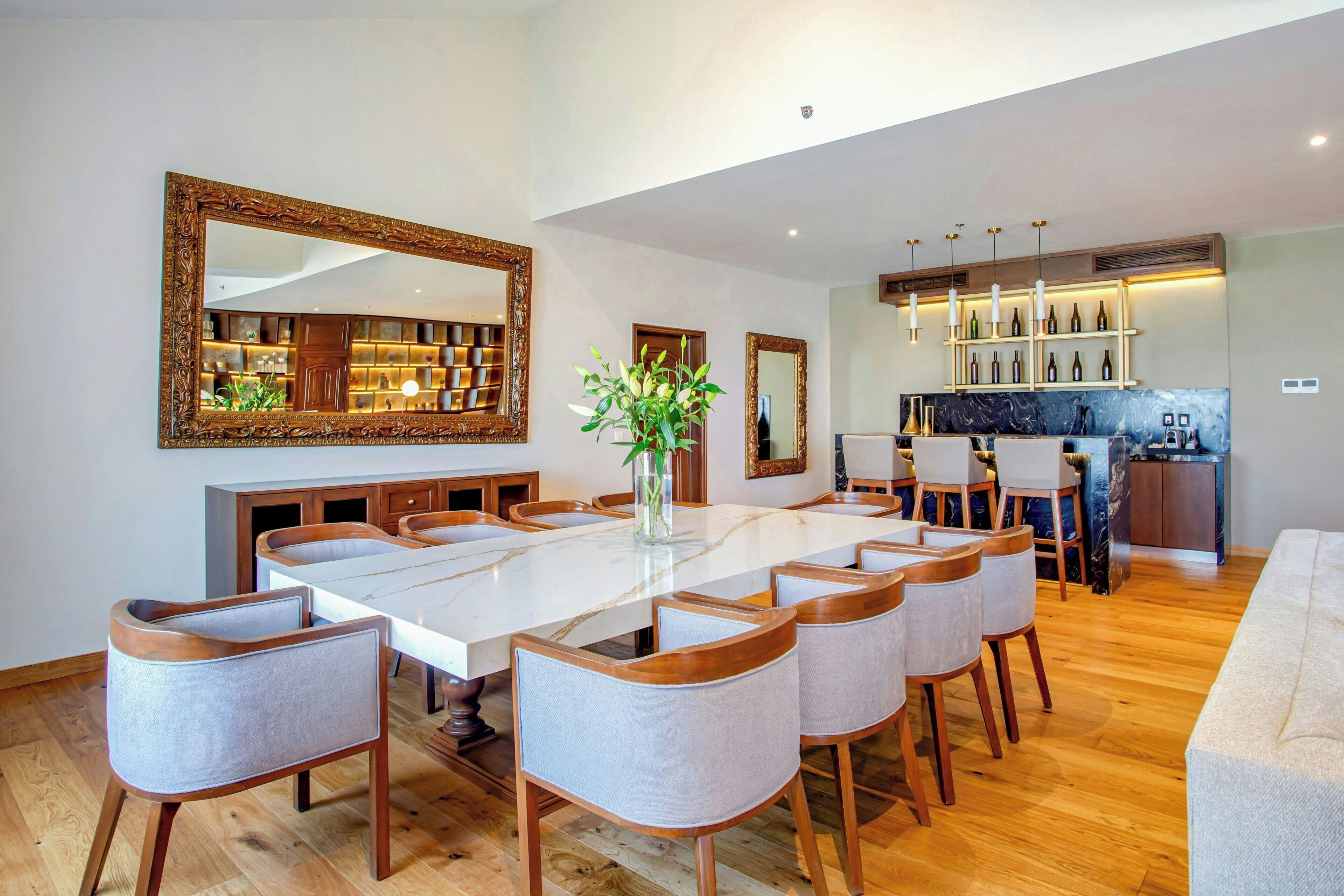 Un comedor amplio con una gran mesa de mármol, sillas de madera y un florero con flores.