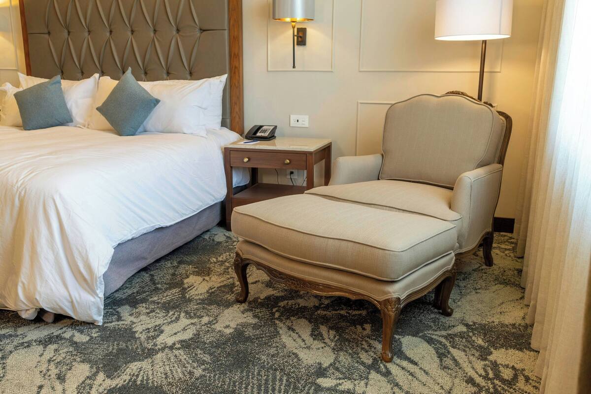 A hotel room with a bed, a chair, a nightstand, and a lamp.