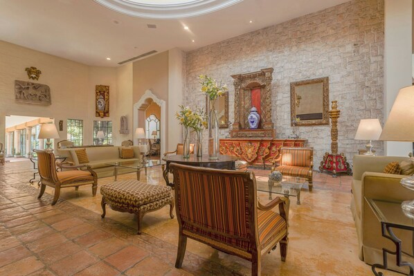 A spacious lobby with a stone wall, classic furniture, and a central decorative area with a vase and mirror.