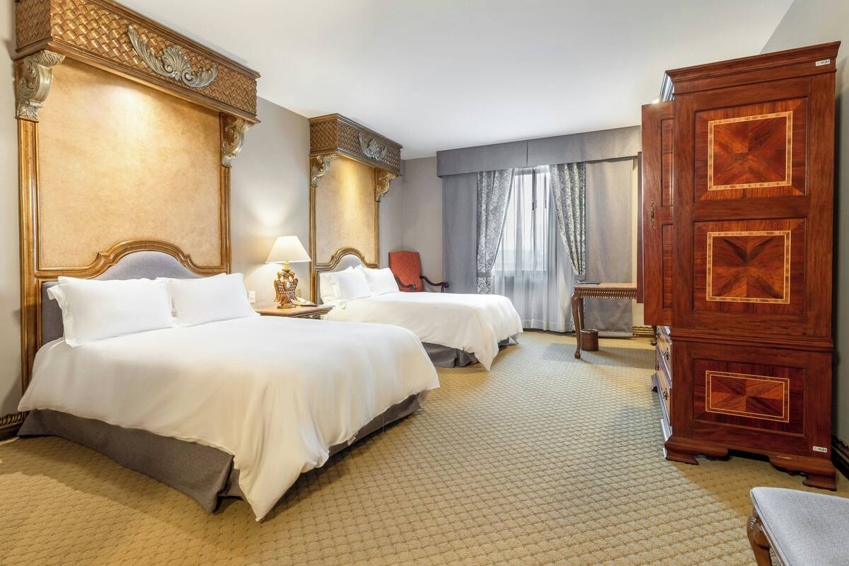 A hotel room with two beds, a large wooden wardrobe, and a chair.