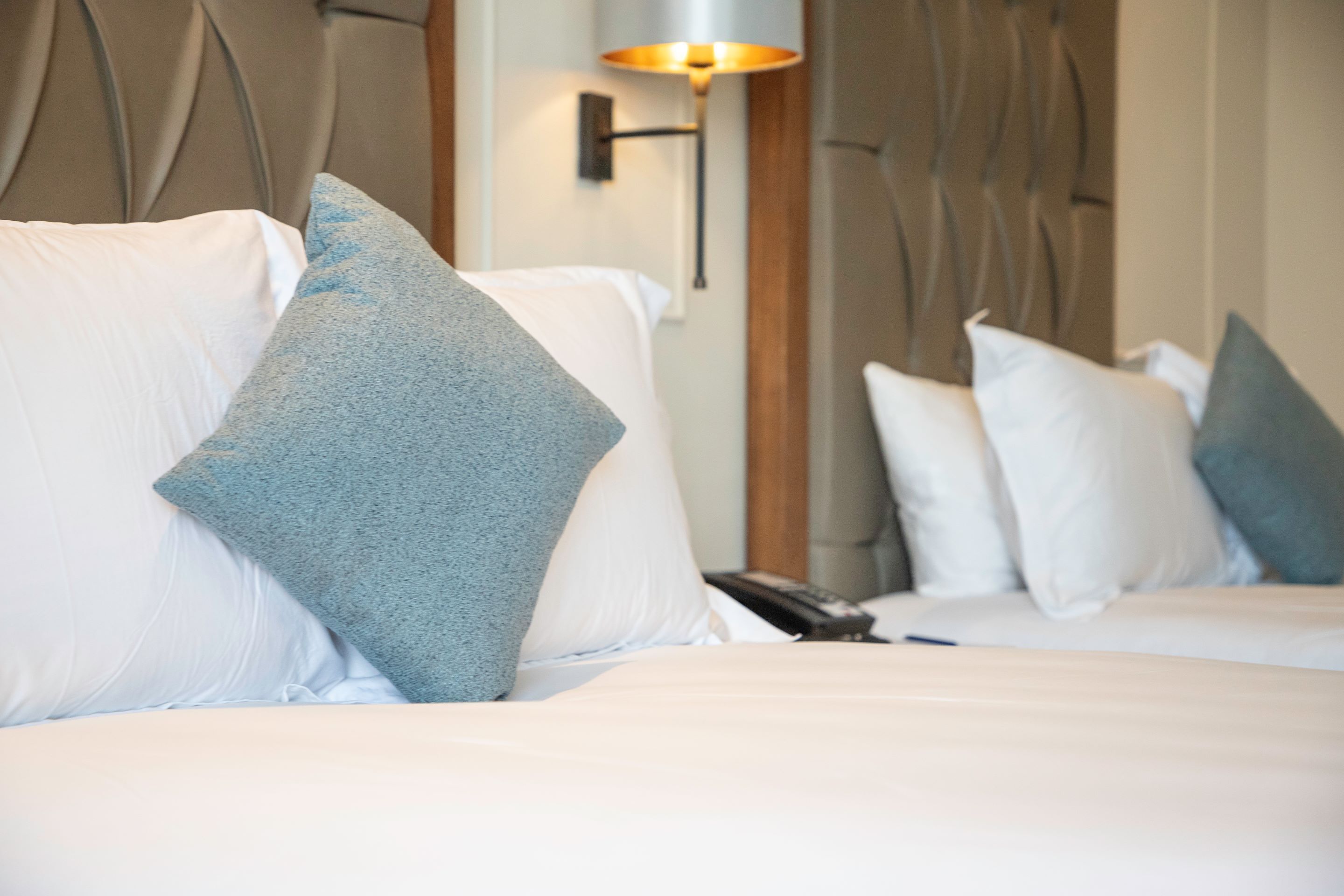 A hotel room with a bed, pillows, a lamp, and a telephone.