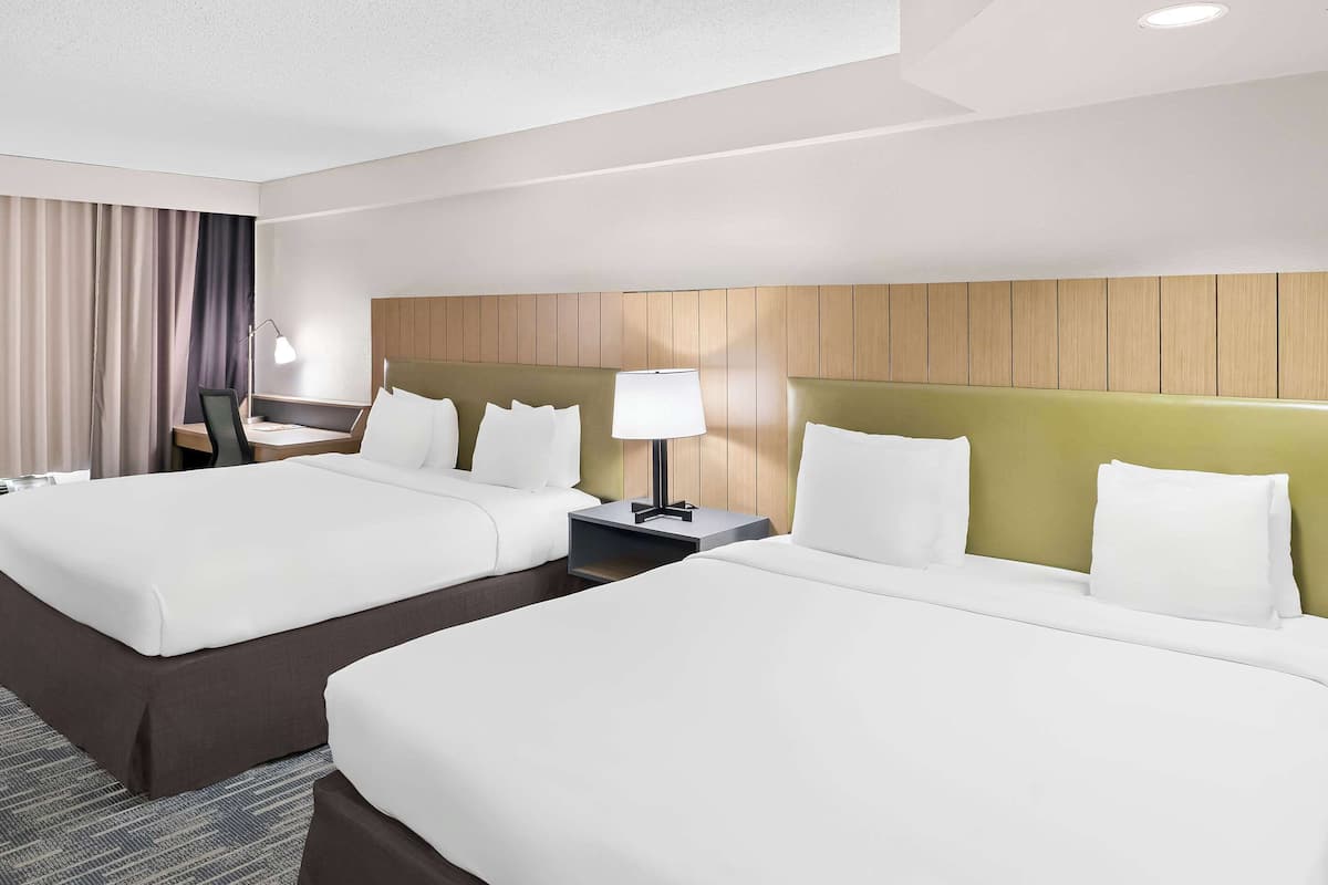 A hotel room with two beds, a desk, a lamp, and a headboard with a wooden panel design.