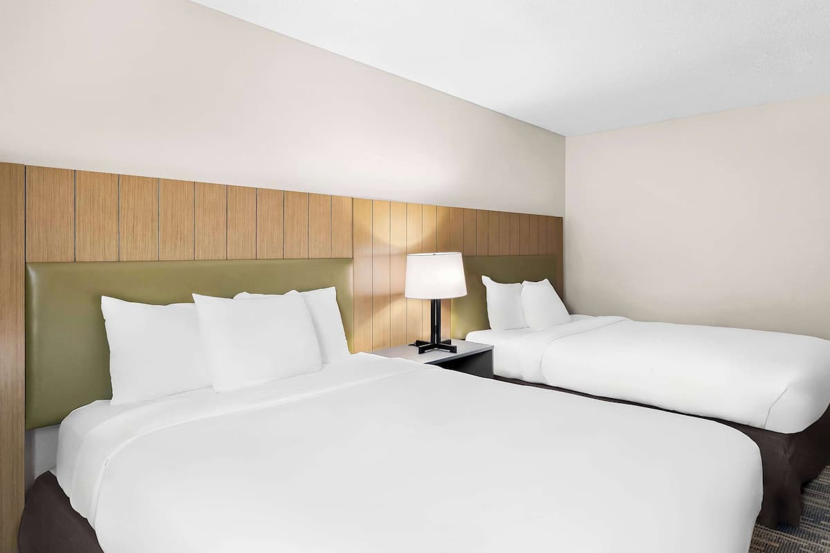 A hotel room with two beds, a nightstand with a lamp, and a wooden headboard.