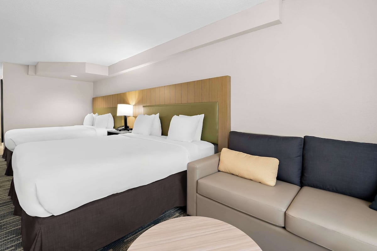 A hotel room with a large bed, a sofa, a bedside table with a lamp, and a headboard.