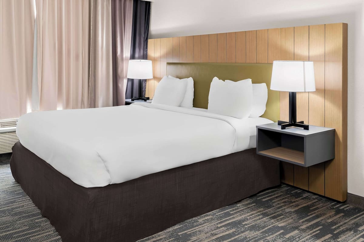 A hotel room with a large bed, two bedside tables with lamps, a wooden headboard, and a carpeted floor.