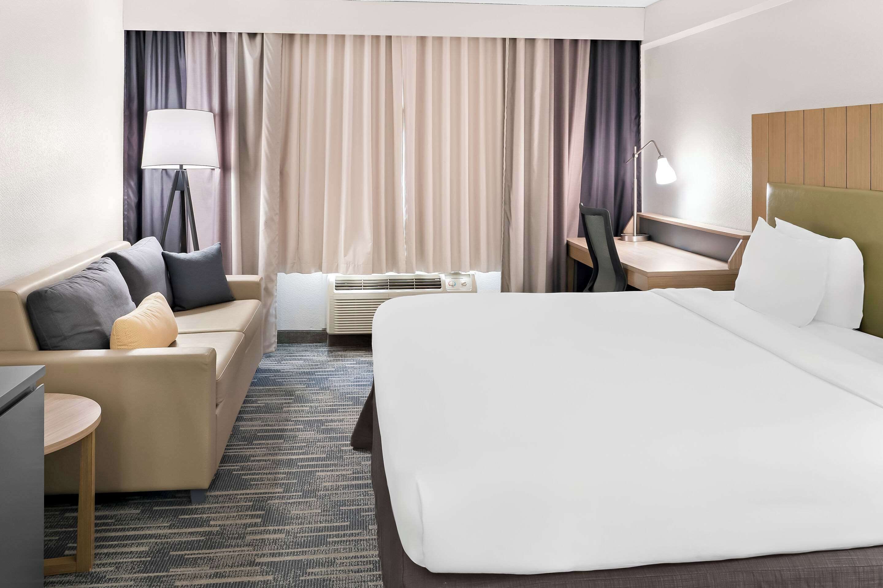 Hotelkamer met een bed, bureau, stoel, bank, lamp en raam met gordijnen.