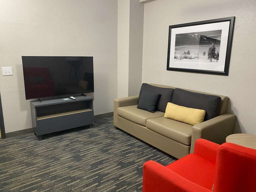 En moderne stue med et fladskærms-tv, en beige sofa med puder og et billede i ramme på væggen.