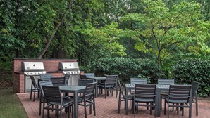 An outdoor patio with a brick floor, surrounded by greenery and trees.