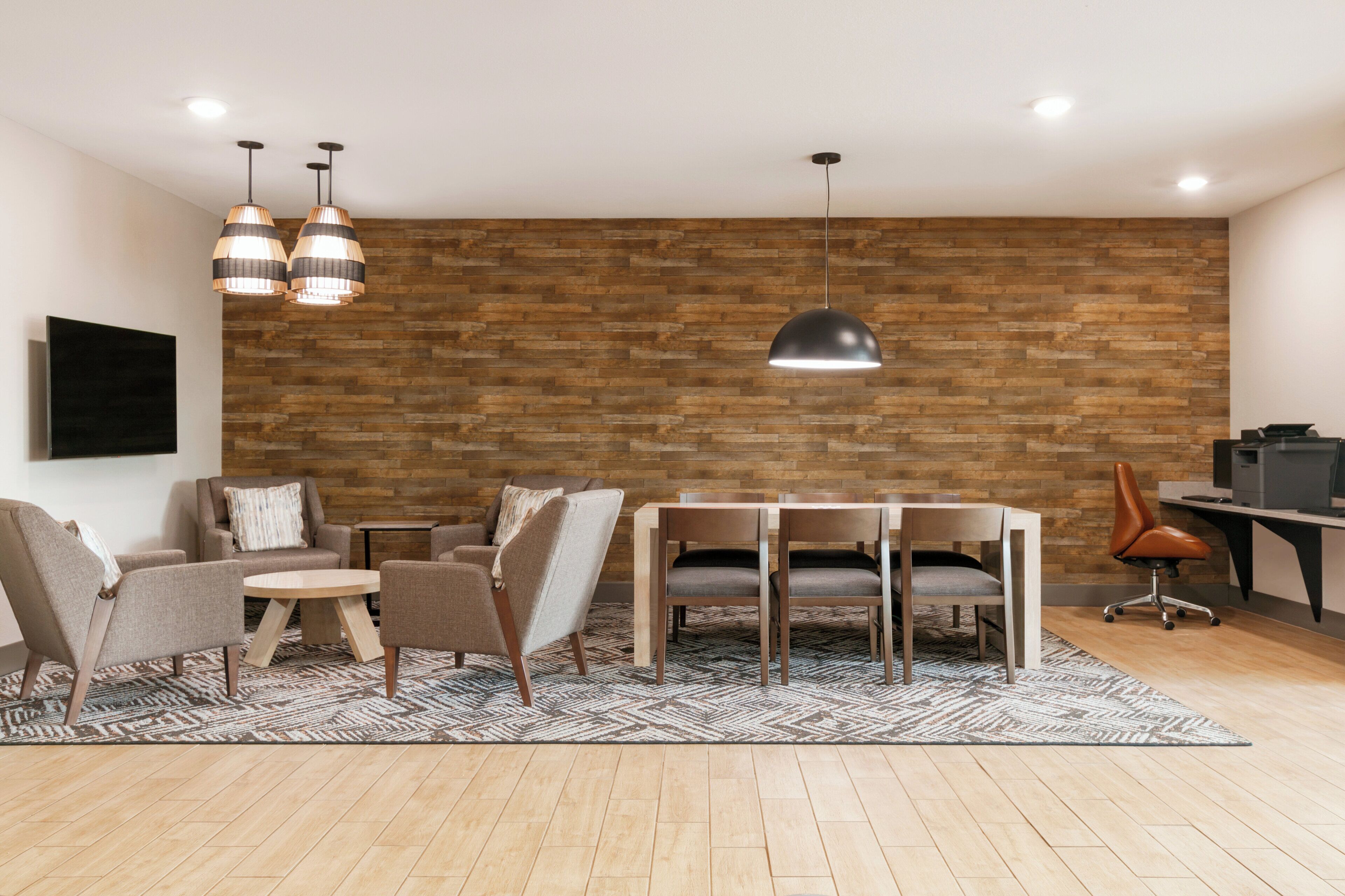 A modern living room with a wooden wall, a dining table, chairs, a sofa, and a TV.