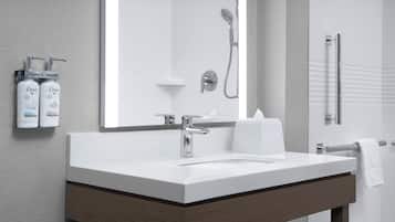A modern bathroom with a large mirror, a white sink, a shower, and two Dove lotion dispensers.