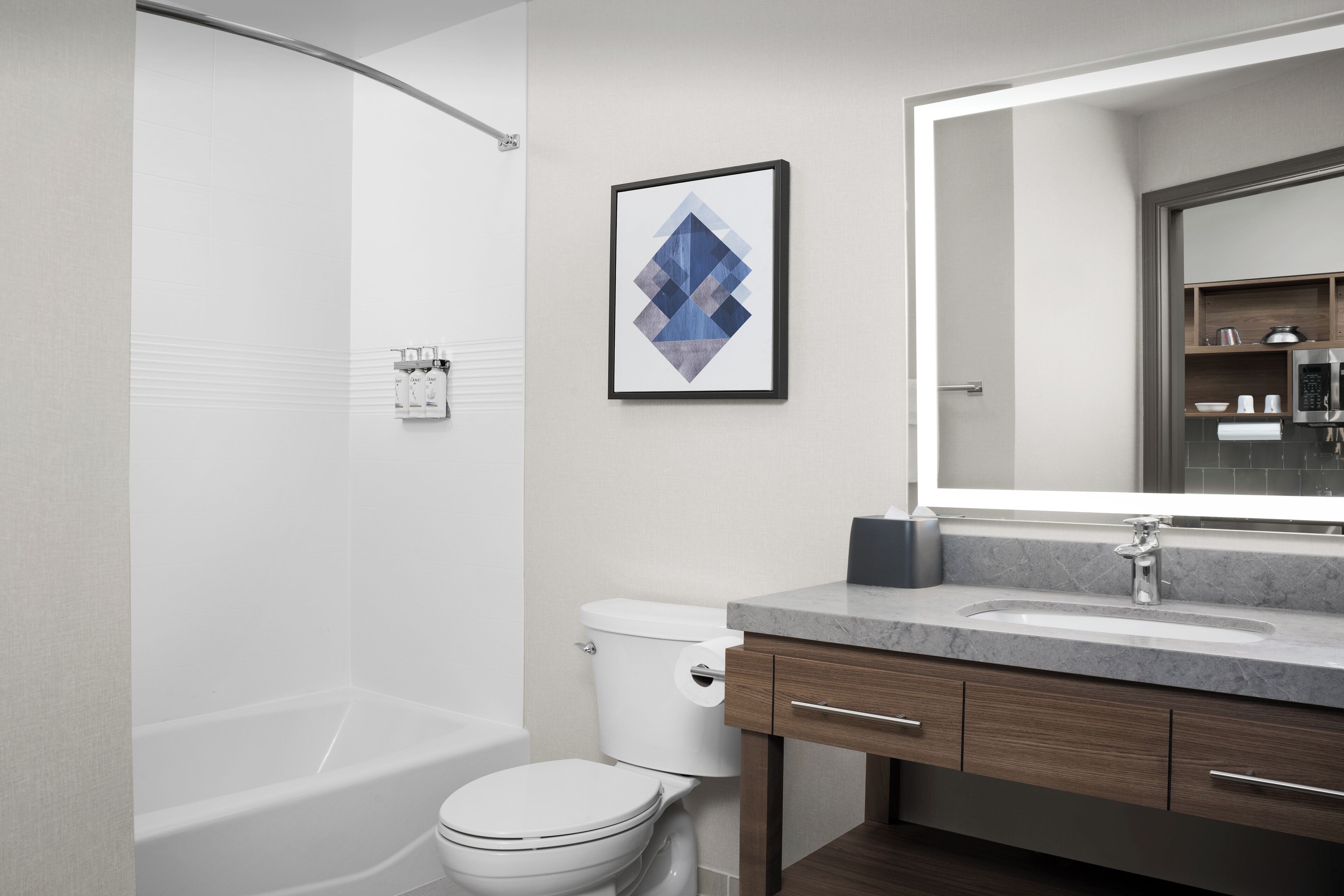 Un baño moderno con bañera, inodoro y tocador con un espejo grande.